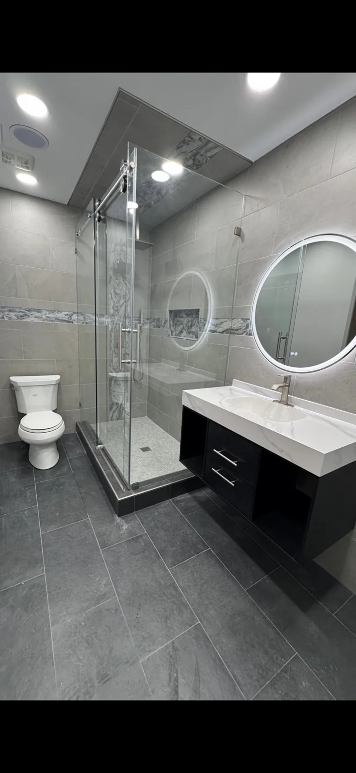 Bathroom renovation with glass shower and circular illuminated mirror